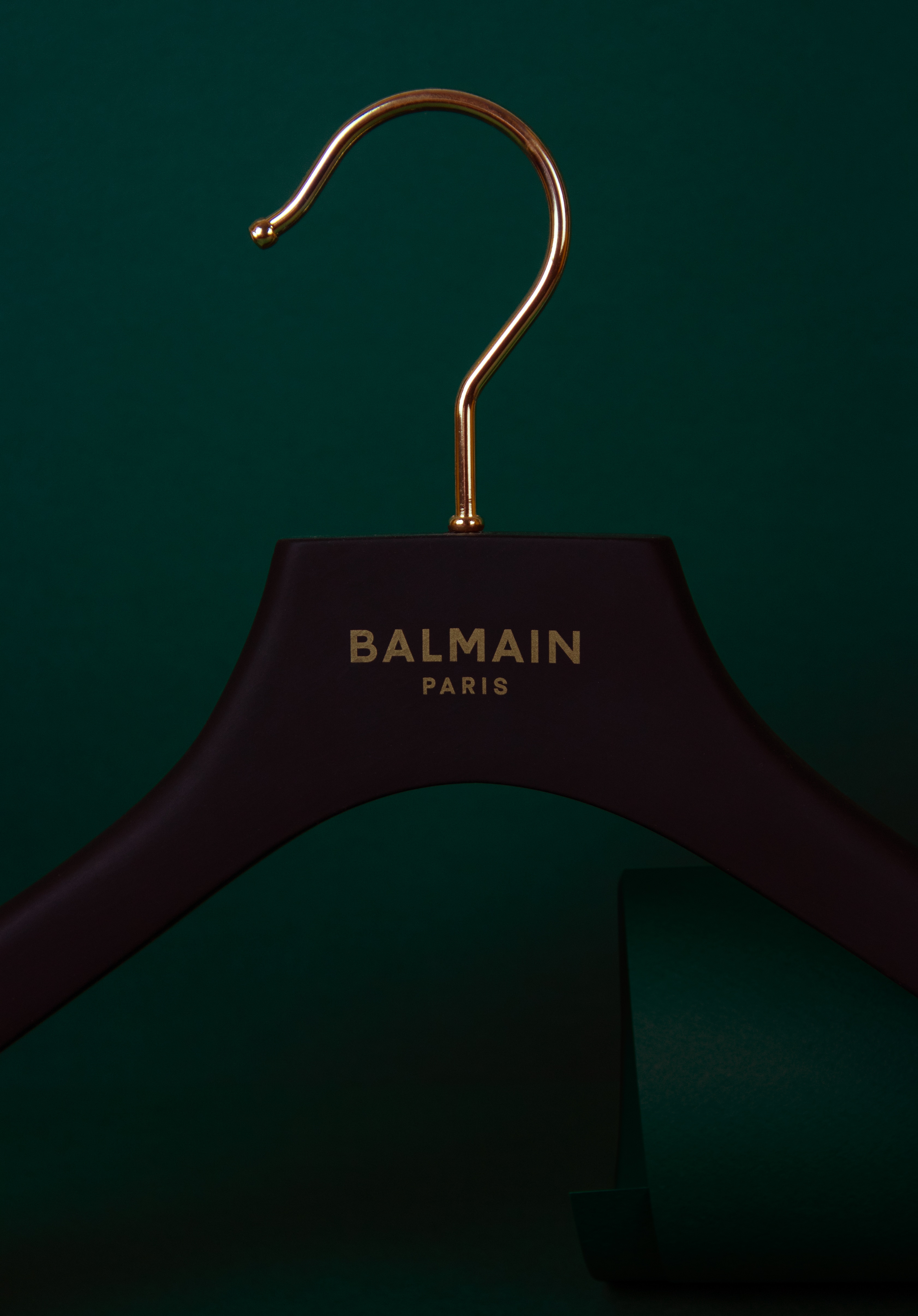 Cintre noir en bois avec logo et crochet finition dorée, de marque Balmain.